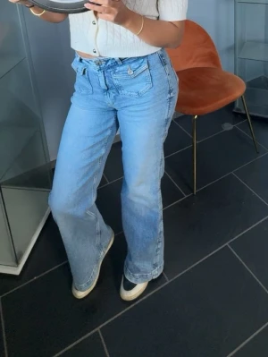 Ljusblå bootcut jeans - Säljer ett par ljusblå bootcut jeans med hög midja och klassiska fem fickor. Jeansen har en avslappnad passform och är tillverkade i denim. Perfekta för en chill och trendig look. Helt nya och använda en gång