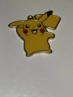Pikachu emaljberlock i gult - Cool Pikachu-berlock i emalj med glada färger. Framsidan är gul med svarta och röda detaljer, baksidan är i metall. Perfekt som hänge till halsband, armband eller nyckelring för dig som gillar Pokémon.