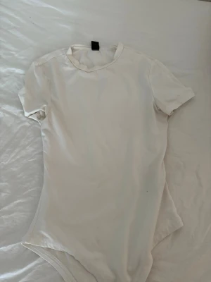 Vit kortärmad body - En enkel och stilren vit body med korta ärmar och rund hals. Perfekt att matcha med jeans eller kjol för en clean look. Tillverkad i mjukt stretchigt material som sitter skönt mot kroppen.