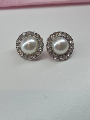 Runda örhängen med pärlor och stenar - Snygga runda örhängen med vita pärlor i mitten och gnistrande klara stenar runt om. Metall i silverfärg ger en elegant look. Perfekta för dig som gillar klassiska accessoarer med lite extra bling.