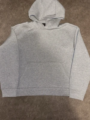 Scuba Hoodie - En stilren ljusgrå hoodie med klassisk huva och stor magficka framtill. Hoodien har ribbade muddar vid ärmslut och nederkant. Perfekt för en avslappnad och enkel look. Tillverkad i mjukt sweatshirtmaterial.
