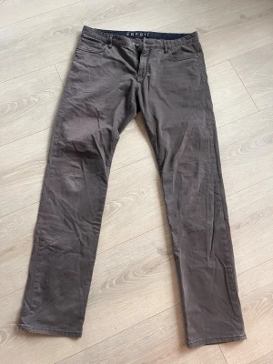 Bruna chinos från Esprit - Snygga bruna chinos från Esprit med klassisk rak passform och fem fickor. Tillverkade i mjuk bomull som känns skön mot huden. Perfekta för dig som vill ha en clean och enkel look. Bälteshällor och knappgylf upptill. Storlek 33/34