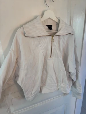 Vit stickad zip hoodie från Lindex - Säljer en oversized vit hoodie från Lindex med ribbad hög krage och guldfärgad dragkedja med ringdetalj. Hoodien har långa ärmar och är gjord i mjukt sweatshirtmaterial. Perfekt för en chill och avslappnad stil.
