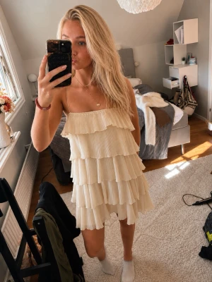 volangklänning ljus beige - Säljer en superfin kort klänning i beige med tunna axelband och flera lager plisserade volanger. Klänningen har en luftig och flowy känsla, perfekt för varma sommar dagar!!! I storlek S! Köpt utomlands❤️❤️