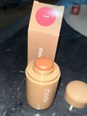 Rhode rouge stick Freckle - Krämrouge i stickformat från Rhode i nyansen Freckle. Färgen är en varm, brunrosa ton som ger ett naturligt glow. Enkel att applicera direkt på kinderna och smälter fint in i huden. Perfekt för dig som gillar en fräsch och naturlig look.