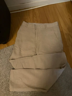 Beige linnebyxor med raka ben - Snygga beige linnebyxor med raka ben och klassisk passform. Byxorna har bälteshällor och sidofickor, perfekta för en avslappnad och stilren look. Tillverkade i ett luftigt linnematerial som passar perfekt till sommaren.