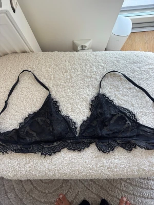 Svart spets-bralette med tunna band - Snygg svart bralette i genomskinlig spets med tunna, justerbara axelband och dekorativ kant. Perfekt för chill dagar hemma eller som ett extra lager under en oversized hoodie. Materialet är mjukt och följsamt med fina spetsdetaljer.