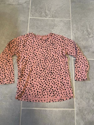 Rosa långärmad topp med leopardmönster - Säljer en rosa långärmad topp från Lindex för barn med svart leopardmönster. Tillverkad i mjuk bomull som känns skön mot huden. Perfekt för dig som gillar djurmönster och vill ha en bekväm och snygg vardagstopp.