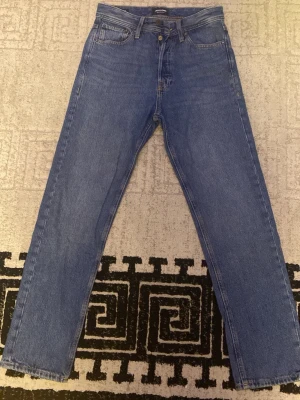 Klassiska raka blå jeans från Jack and Jones  - Ett par klassiska blå jeans med rak passform och fem fickor. Jeansen har normalhög midja och är tillverkade i denim. Perfekta för en avslappnad och tidlös look.