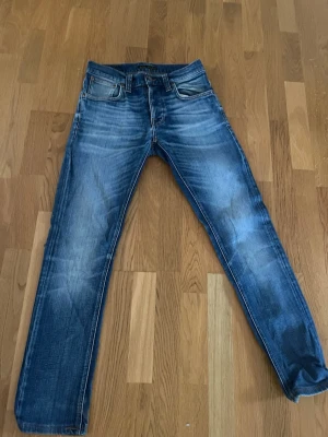 Nudie jeans  - Snygga blå nudie jeans med slitna detaljer och klassisk femficksdesign. Jeansen har raka ben och ljusare partier framtill och baktill för en cool, använd look. Materialet är denim och passformen är normal. Perfekta för en avslappnad stil. Storlek W29 L32