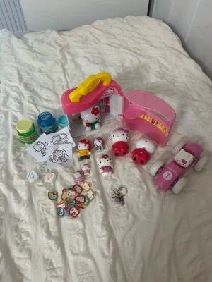 Hello Kitty licensed-lekset med tillbehör - (HELLO KITTY LICENSED) Samling med Hello Kitty-leksaker, inklusive rosa bil, figurer, klistermärken, nyckelring, små burkar, färgläggningsbilder och ett rosa hus. Allt har söta Hello Kitty-motiv och färgerna går i rosa, vitt, rött och blått. Perfekt för dig som älskar Sanrio och vill ha ett komplett set.