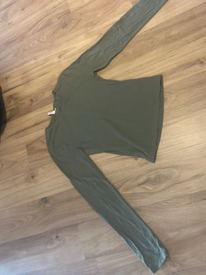 Olivgrön långärmad topp från Nelly - Säljer en enkel och stilren olivgrön långärmad topp från Nelly. Toppen har en rund halsringning och är gjord i mjuk bomull, perfekt att matcha med jeans eller kjol för en clean look.