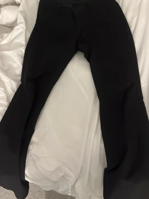 Svarta utsvängda kostymbyxor low waist - Säljer ett par svarta kostymbyxor med utsvängda ben. Byxorna har en klassisk midja och stilren design utan synliga detaljer. Perfekta för dig som gillar en clean och modern look.