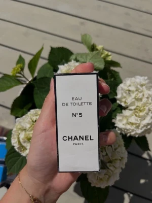 Chanel N°5 Eau de Toilette - Klassisk Chanel N°5 Eau de Toilette i elegant vit och svart förpackning med stilren design. Parfymen är ikonisk och passar dig som vill ha en tidlös och lyxig doft. Boxen har tydlig Chanel-logga på toppen och är tillverkad av kartong.