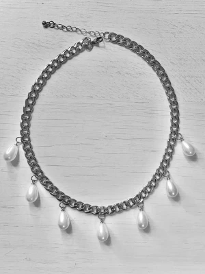 Silverfärgat halsband med pärldroppar - Snyggt halsband i silverfärgad rostfritt med sju vita droppformade pärlor som hänger längs kedjan. Kedjan har större länkar och justerbar längd med karbinlås. Perfekt för att ge en trendig touch till din outfit.