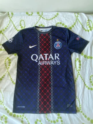PSG matchtröja  - Snygg PSG matchtröja i mörkblått med rött och vitt mönster framtill. Tryck med Qatar Airways och PSG-logga på bröstet, samt O. Dembélé och nummer 10 på ryggen. Tillverkad i lätt och ventilerande material, perfekt för fotbollsträning eller match.