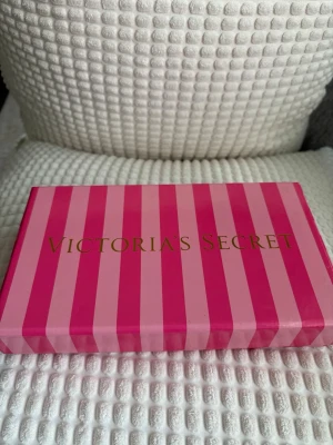 Rosa kuvertväska Victoria's Secret - Snygg rosa kuvertväska från Victoria's Secret med guldfärgad logga framtill. Väskan har en stilren och enkel design i ett strukturerat material. Perfekt för dig som vill ha en färgklick till outfiten och gillar trendiga accessoarer.
