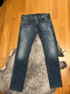 Replay hyperflex jeans - Säljer ett par blå jeans från Replay med slitningar och distressed detaljer på framsidan. Jeansen har klassisk femficksmodell, normal midja och smal passform. Perfekta för en avslappnad och trendig look.