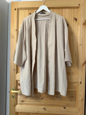Beige oversized kimono cardigan - Luftig och oversized kimono-inspirerad cardigan i beige. Tillverkad i ett mjukt, vävt material med trekvartsärmar och öppen front. 