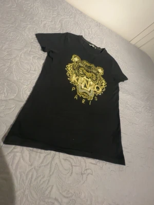 Svart t-shirt med guldtigertryck - Snygg svart t-shirt med ett stort guldfärgat tigertryck och texten 'PARIS' framtill. T-shirten har korta ärmar och en klassisk passform. Perfekt för dig som vill sticka ut med ett coolt motiv.