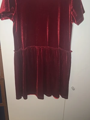Vinröd sammetsklänning kort ärm - Mysig vinröd sammetsklänning med korta ärmar och rund hals. Klänningen har en markerad midja och faller i en ledig, kort siluett. Perfekt för dig som gillar mjuka material och en klassisk look.