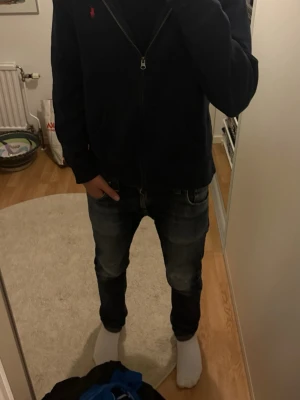 Mörkblå hoodie från Polo Ralph Lauren - Mörkblå hoodie med dragkedja från Polo Ralph Lauren. Klassisk design med röd broderad logga på bröstet och mjukt material. Perfekt för en chill och stilren look.
