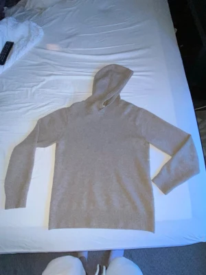 Beige stickad hoodie - Mysig beige stickad hoodie med lång ärm och ribbade muddar. Hoodien har en enkel och clean design utan tryck eller dragkedja, perfekt för en avslappnad stil. Materialet är mjukt och skönt.
