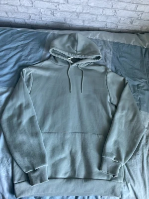 Ljusgrå hoodie med huva - En stilren ljusgrå hoodie med huva och dragsnören. Hoodien har en klassisk känguruficka framtill och ribbade muddar vid ärmslut och nederkant. Perfekt för en avslappnad och trendig look.