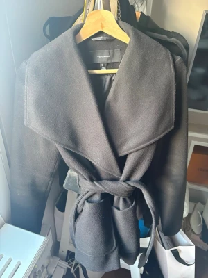 Svart kappa Vero Moda - Stilren och varm svart kappa från Vero Moda. Har en stor, snygg krage, långa ärmar och knytband i midjan som gör att man kan forma passformen efter sig. Har fickor på framsidorna. Kappan är längre i modellen och täcker nästan hela rumpan, vilket gör den perfekt för hösten 🍂   Snygg och lättmatchad  Varm och mysig – perfekt för kyligare höstdagar  Knytband i midjan för en mer figurnära look  Storlek S  Svart  Använd men i jättefint skick, ser ut som ny  Inga defekter eller märkbart slitage