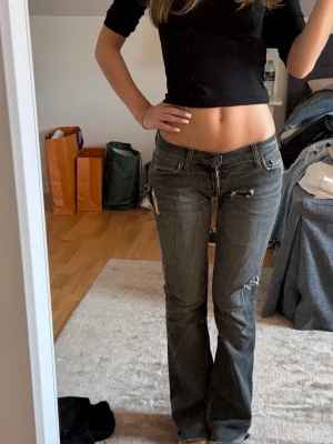 Grå slitna bootcut jeans - Säljer ett par grå bootcut jeans med slitningar och råa detaljer. Jeansen har låg midja, fem fickor och dekorativa sömmar på bakfickorna. Perfekta för en avslappnad och trendig look. Perfekta low waist jeans.mina favoriter❤️❤️❤️❤️