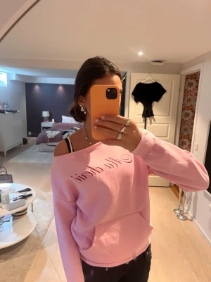 Rosa off shoulder sweatshirt med text Ma chérie - Säljer en ljusrosa sweatshirt med trycket 'Ma chérie' i skrivstil framtill. Tröjan har en bred, off-shoulder ringning och en stor magficka. Mjuk bomullskänsla och ribbade muddar vid ärmslut och nederkant. Perfekt för en chill och trendig look.💖