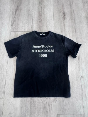 Svart Acne Studios t-shirt -  svart t-shirt från Acne Studios med vit text 'STOCKHOLM 1996' på bröstet. Klassisk passform och rund halsringning. Perfekt för dig som gillar stilrena och trendiga plagg.