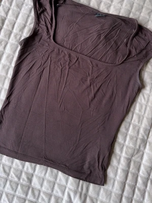 Brun ärmlös linnetopp - Snygg brun ärmlös linnetopp med fyrkantig ringning. Toppen är i mjukt material och har en enkel, stilren design som passar perfekt till jeans eller kjol.