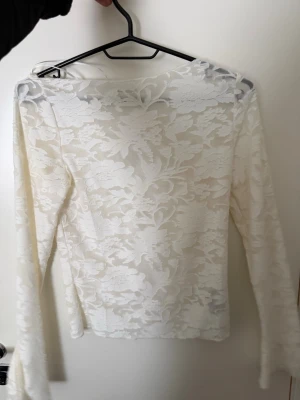 Vit spets blus - Snygg vit blus i genombruten spets med blommigt mönster. Långärmad och figurnära passform, perfekt att styla lager på lager eller som den är. Tillverkad i polyester för en lätt och luftig känsla. (PRIS LAPP KVAR)