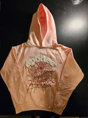 Rosa Sp5der Web Hoodie – L - Rosa hoodie med stort spindelnätsmotiv, upphöjda vita detaljer och små stjärndetaljer. Snygg streetwear-design med huva och känguruficka. Helt oanvänd och i nyskick. Förvarad i skyddspåse. Se bilder för detaljer.