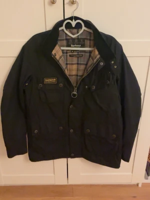 Barbour International Wax Jacket M – Svart - Säljer en Barbour International Wax Jacket i storlek M. Klassisk modell med vaxad yta, tartanfoder och ikonisk Barbour International-logga. Stilren svart färg som passar till det mesta.  Modell: MWX0958 Storlek: M Färg: Svart Material: Waxed cotton  Knappast använd och i väldigt fint skick. Inga hål eller större skador. Se bilder för skick och detaljer.  Sökord: Barbour, Barbour International, Barbour jacket, Barbour wax jacket, Barbour jacka, Barbour M, waxed jacket, wax cotton, vaxjacka, herrj