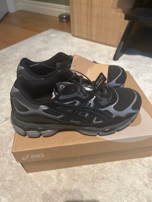 Svarta Asics sneakers med grå detaljer - Snygga svarta sneakers från Asics med grå och svarta detaljer. Skorna har en sportig design med mesh och syntetmaterial för bra andningsförmåga och komfort. Perfekta för dig som gillar stilrena och funktionella sneakers.