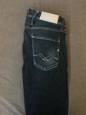 Reaplay anbass jeans  - Snygga mörkblå jeans från Replay (modell: anbass) med klassisk femficksmodell och kontrastsömmar. Jeansen har en diskret tvättad look och detaljerade sömmar på bakfickan. Perfekta för dig som gillar stilrena och tidlösa jeans.