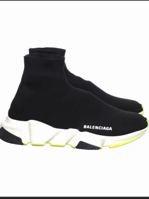 Balenciaga Speed Trainer svarta sneakers - Svarta Balenciaga Speed Trainer sneakers med stickad strumpdesign, vit chunky sula och neongula detaljer undertill. Loggan syns på sidan. Skorna är lätta och flexibla med en modern siluett som sticker ut.