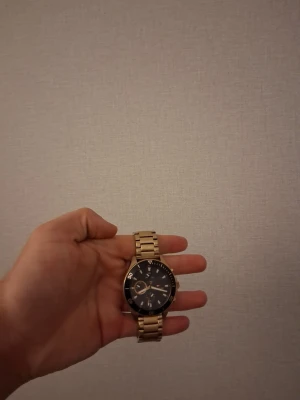 Tommy Hilfiger Klocka FUNKAR EJ - Säljer en snygg klocka med guldfärgat metallarmband och mörk urtavla. Klockan har tydliga siffror och markeringar runt boetten samt en klassisk länkdesign. Perfekt accessoar för dig som vill ha en stilren look. FUNKAR EJ men gå till närmsta klock butik så löser dem resten inte DYRT 