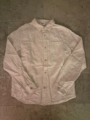 Beige linneskjorta från Kappahl - Säljer en stilren beige skjorta från Kappahl i storlek 152. Skjortan är tillverkad i linne, har klassisk krage, bröstficka och knappar framtill. Perfekt för dig som gillar en enkel och fräsch look.