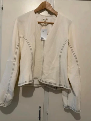 Vit långärmad topp med kontrastsömmar - Vit långärmad topp med v-ringning och markerade kontrastsömmar som ger en cool och modern look. Toppen har en något boxig passform och är tillverkad i ett mjukt bomullsmaterial. Perfekt att styla med jeans eller kjol.