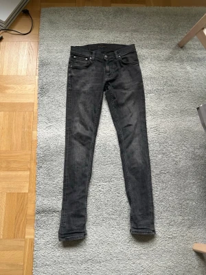 Svarta nudie jeans - Snygga svarta slim fit jeans med klassisk femficksdesign och smal passform. Jeansen har en något tvättad look och raka ben. Perfekta för dig som gillar en stilren och enkel look. Priset kan även diskuteras🔥🙌 Storlek 29/32 