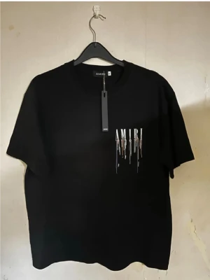Svart AMIRI t-shirt  - Snygg svart t-shirt från AMIRI med coolt tryck framtill där märkesnamnet droppar i olika färger. Klassisk rund hals och korta ärmar. Perfekt för dig som vill ha en stilren men ändå unik look.