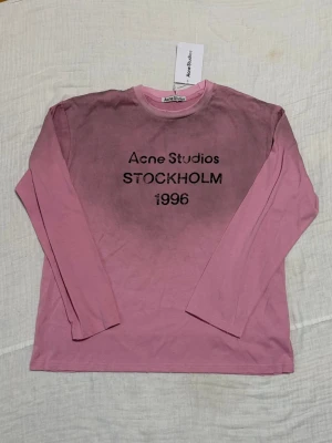 Långärmad rosa t-shirt Acne Studios - Säljer en långärmad rosa t-shirt från Acne Studios med trycket 'STOCKHOLM 1996' på bröstet. Tröjan har en klassisk rund hals och är gjord i mjuk bomull. Perfekt för dig som gillar streetwear och vill ha något unikt i garderoben.
