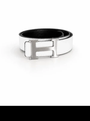 Vitt skärp med silverfärgat H-spänne - Snyggt vitt skärp med ett stort, silverfärgat H-format spänne. Skärpet har en stilren design med svarta kanter och insida. Perfekt accessoar för att lyfta din outfit med en clean och modern look.