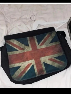 Datorväska med Union Jack-tryck - Snygg datorväska i svart tyg med stort Union Jack-tryck på locket. Väskan har axelrem och klassisk messenger-modell, perfekt för laptop och skolgrejer. Det får plats laptop, matlåda, och annat (den är större än en laptop)