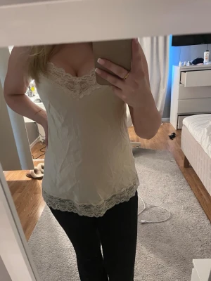 Beige spetslinnetopp med smala band från Intimissimi storlek S  - Säljer en beige siden topp med tunna axelband och vacker spetsdetalj vid ringningen och nederkanten. Toppen har en feminin v-ringad form och är perfekt för lager på lager eller sommarens varma dagar eller som nattlinne. Från Intimissimi storlek S