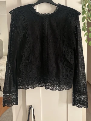 Svart spetsblus med långa ärmar - Elegant svart spetsblus med långa ärmar och vackra spetsdetaljer längs kanterna. Blusen har rund halsringning och dekorativa mönster i spetsen. Har inte kommit till användning därför den säljs💕💕
