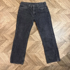 Svarta 514 Levi's  - Säljer ett par svarta jeans med rak passform och klassisk femficksdesign. Jeansen har en vintage-tvättad look och synliga sömmar. Materialet är denim i bomull och de har bälteshällor samt knappgylf. Perfekta för en avslappnad streetwear-stil.
